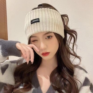 Cream ribbed knit sports headband with logo tag for women shown on a model