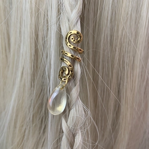 Detail of golden spiral hair coil with clear teardrop pendant braided into blonde hair