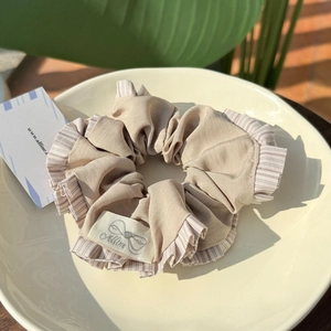Close-up of beige striped pleated scrunchie with brand tag on a ceramic plate