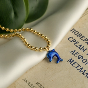 Macro shot of gold-plated bead chain with a blue dolphin enamel pendant on vintage silk