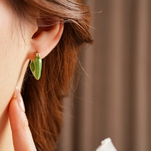 Model wearing a vintage gold-tone hoop earring featuring a green enamel heart pendant