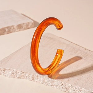 Macro detail of amber resin C-shape open bracelet on a natural stone background