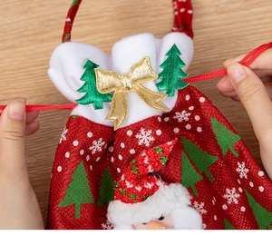 Close-up of hands pulling red drawstrings on a Santa themed velvet gift bag with gold bow