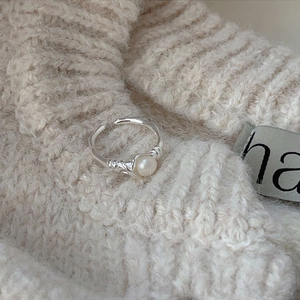 Macro detail of adjustable silver ring with twisted band and pearl on knit background
