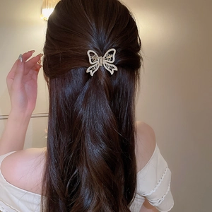Detailed view of a gold butterfly hair claw with pearls on elegant half-up brunette hair