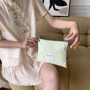 Close-up of a lime green nylon makeup bag with blue zipper held by a model on sofa
