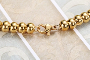 Macro detail of golden bead bracelet featuring a polished lobster clasp closure