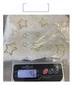 Detailed view of white plush Christmas tree skirt fabric with golden stars on a scale