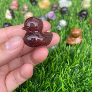 Polished natural crystal duck carving in deep red held against a garden background
