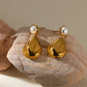 Detailed view of teardrop pearl earrings with gold charms on a natural stone background