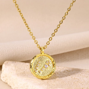 Detail of 18K gold constellation coin necklace with white zircons on textured stone