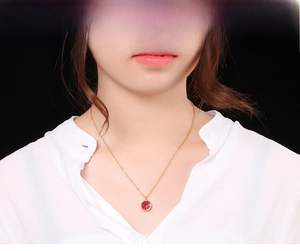 Close-up of a gold-plated necklace with a vibrant round red gemstone pendant on a model