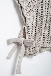 Détail de maille épaisse ajourée avec nœud décoratif latéral sur un pull beige doux
