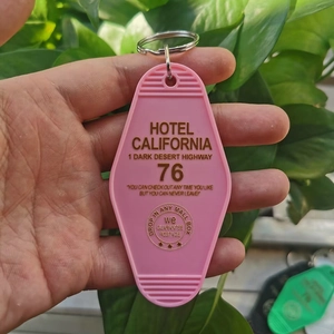 Pink Hotel California plastic keychain with golden text held against green leaves