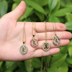 Virgin Mary oval pendant necklace with colorful zircon stones held in palm on green leaf