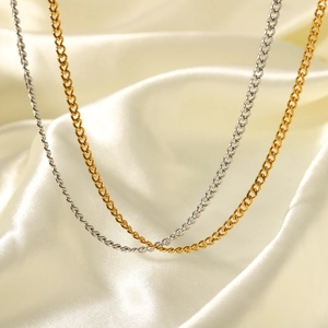 Minimalist stainless steel curb chain necklace in gold and silver on white satin fabric