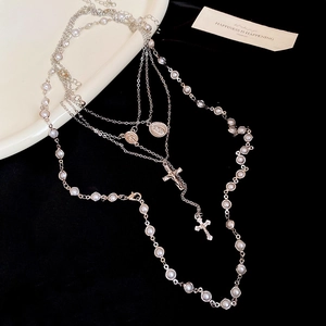 Detail of multi-layered silver necklace with pearls, cross and virgin mary medal charm