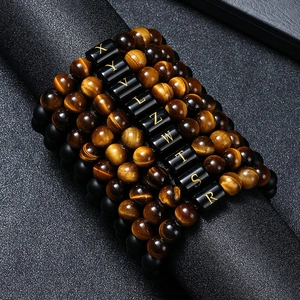 Tiger eye and matte bead bracelets with gold initial letters on a black textured background