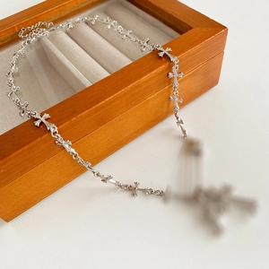 Detail of silver safety pin cross link chain necklace on a wooden jewelry box display