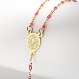 Macro detail of golden rosary necklace with pink resin beads and Saint Benedict medal