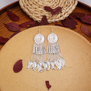 Detailed macro view of Bohemian silver tassel earrings with fish charms on a tray