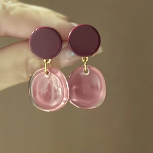 Detail of two-tone purple and pink resin geometric earrings held by hand on dark backdrop