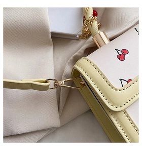 Detail of metal hardware and cherry print pattern on a cream crossbody shoulder bag
