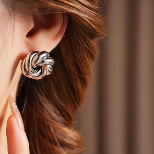 Close-up of silver metal twist swirl earrings worn by a model on a brown background