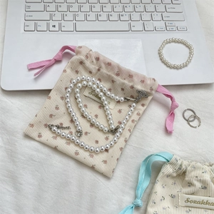 Detail of floral corduroy cosmetic pouch with a pearl saturn pendant necklace
