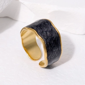 Detail of golden adjustable ring with black enamel inlay on white textured stone background