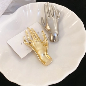 Detailed view of creative hand-shaped brooches in gold and silver finish on a shell tray