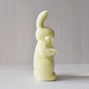 Side view of a cute yellow flocked Easter rabbit figurine with a matching ribbon bow