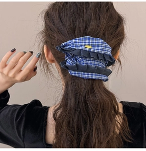 Detail of blue checkered fabric scrunchie with dark ruffled edges and a small yellow tag