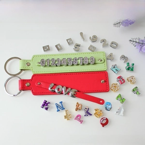 Macro shot of colorful DIY alphabet sliders and faux leather keychains with diamond charms