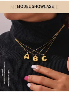 Close-up of golden bubble initial pendants on black knit sweater, pendants only
