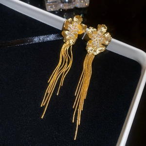 Detailed close-up of 18k gold-plated floral earrings with long tassels and pearls on velvet