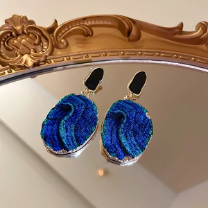 Macro shot of blue resin drop earrings with gold metal edges on a vintage mirror