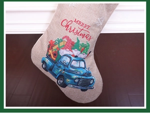 Detail of burlap Christmas stocking featuring a vintage blue truck and gnome design