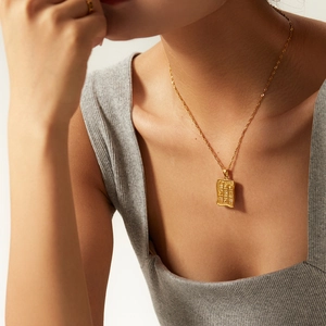 Close-up of a gold rectangle textured pendant with zircons on a twisted rope chain necklace