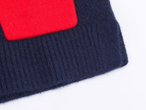 Close-up of deep blue knitted fabric with red patchwork and ribbed sleeve cuff details