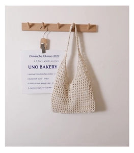 Detail of minimalist cream hollow knit shoulder bag hanging on a wooden wall hook