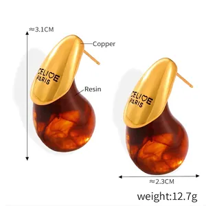 Macro detail of tear-shaped earrings showing golden copper texture and amber resin finish