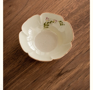 Close-up of hand-painted daisy pattern on ceramic tea strainer with petal edge design