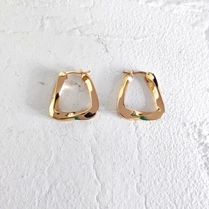 Detailed close-up of golden geometric twist earrings on a white textured surface