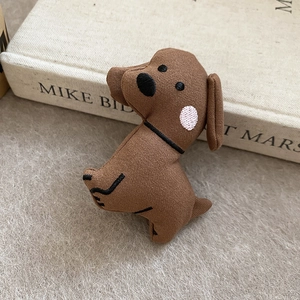Close-up of a brown fabric plush puppy brooch with black embroidery on felt background