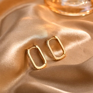 Close-up of gold rectangular U-shaped hoop earrings with paved white zircons on champagne silk