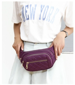 Purple nylon waist bag with quilted stitching and three gold zipper pockets on model