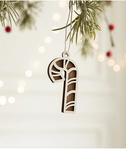Detail of candy cane wooden Christmas ornament hanging on a snowy pine branch