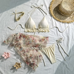 Detailed flat lay of beige ruffled bikini with floral mesh sarong and beach accessories