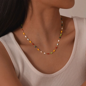 Dettaglio di una collana di perle colorate sul collo di una modella con catena d'oro